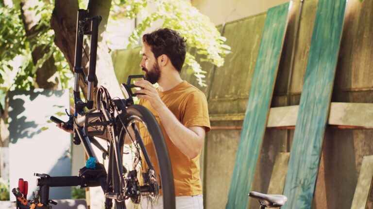 Male cyclist mending bicycle gear outdoors in his yard