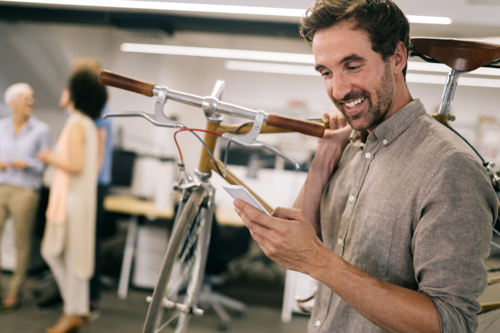 Man checking his smartphone while carrying a bicycle in a modern office workspace