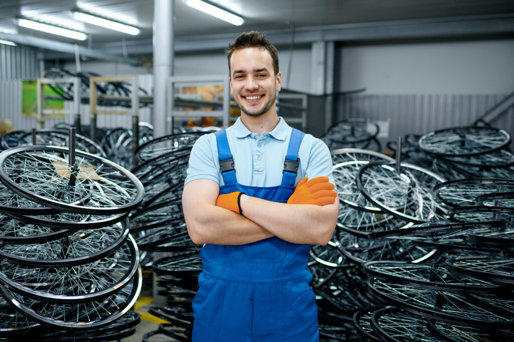 Bicycle mechanic in uniform standing in factory with assembled bike wheels