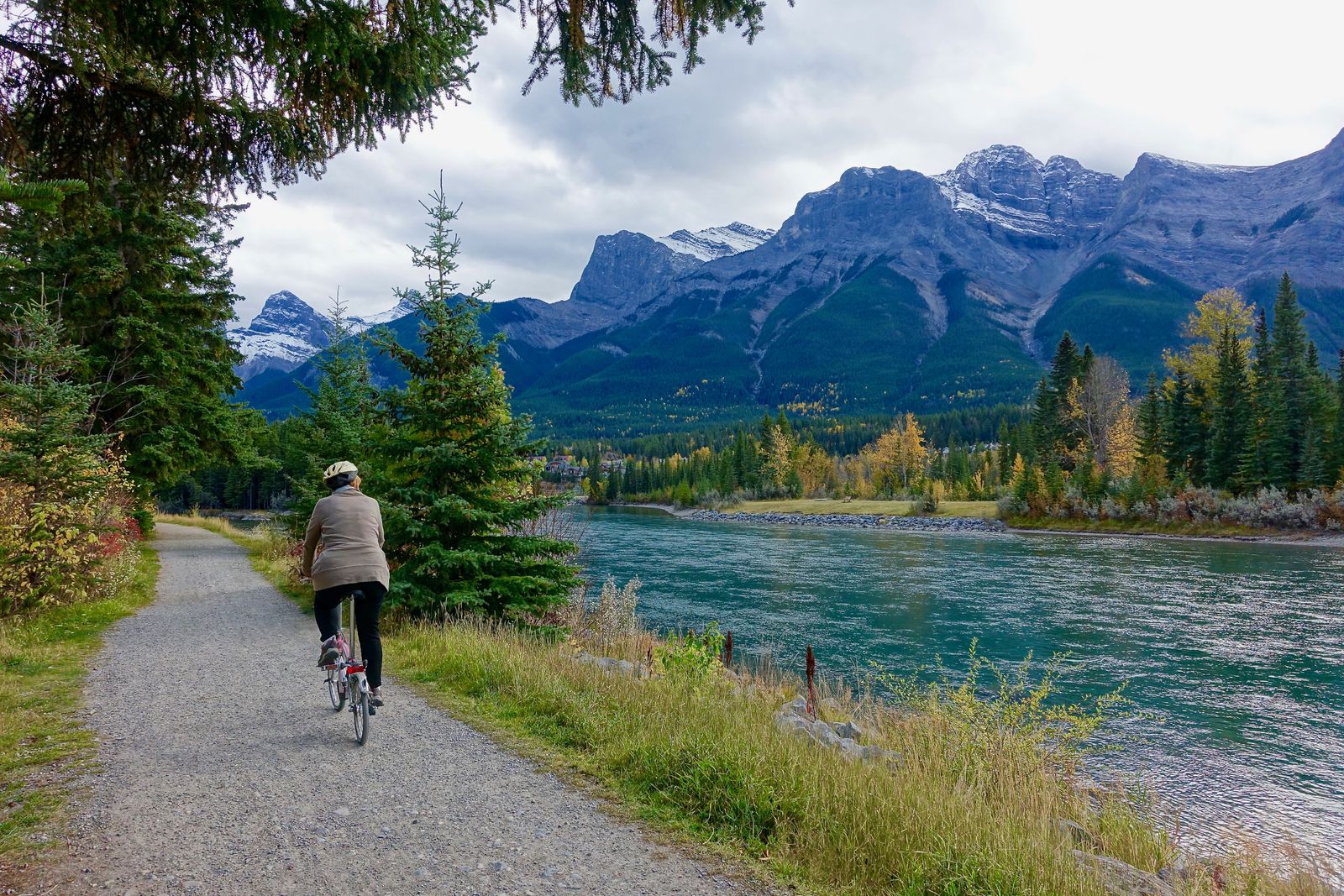 Cyclist riding a scenic gravel trail beside a river surrounded by mountains